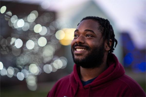 KeJuan Farrell-Bey smiles and looks off to the right, with lit-up trees in the background. 