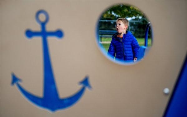  A small child is seen through a circle of playground equipment with a blue anchor on the side. 