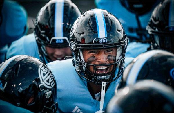  A football player with paint under his eyes lets out a yell while in a huddle. 