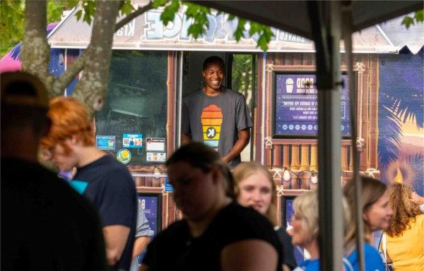  A person standing in the window of a food truck smiles while among a crowd of people. 