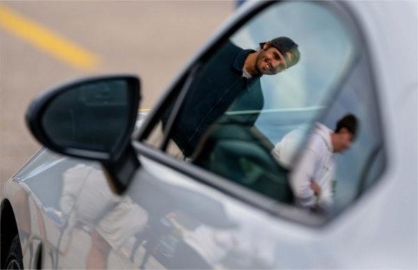  A smiling person is reflected in a car mirror during a car show. 