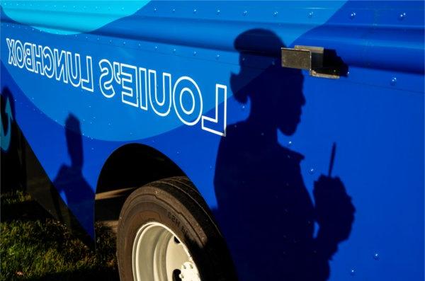  A person holding a drink cast a shadow against a blue food truck. 