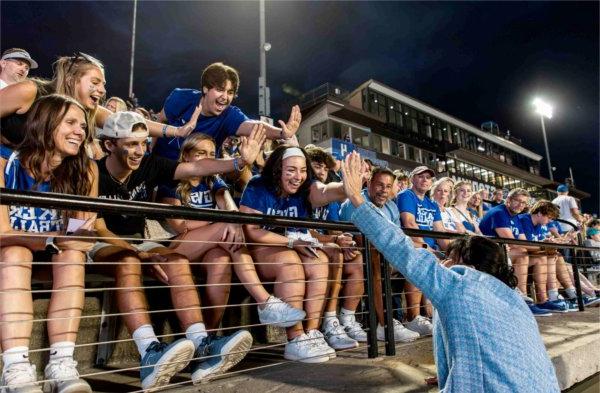  A university president wearing a blue coat high fives students in the stand during a football game.