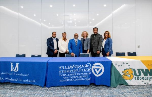 six people standing behind a table with banners from GVSU, Wilberforce and Voorhees universities