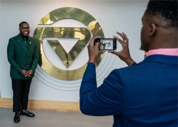 student taking a photo of another student who is standing by the gold GV