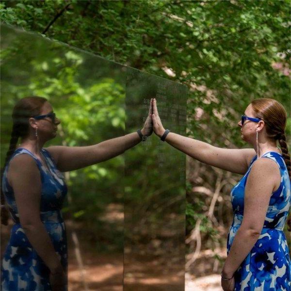 A person places their hand on a stone wall. Their reflection is seen to the right.