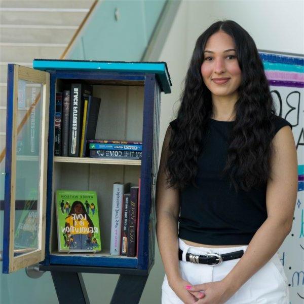 Jordyn Horton stands next to the Black Book Exchange Box in the Mary Idema Pew Library