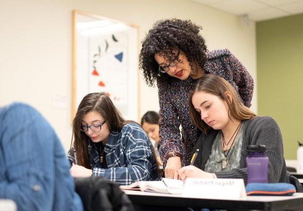 professor leaning over to look at student's paper; two women students seated next to each other