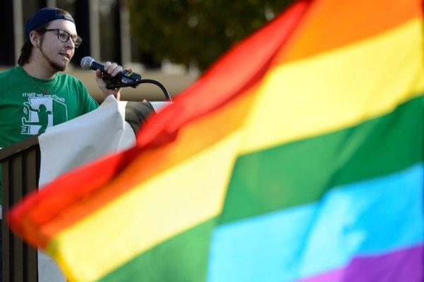 rainbow flag in front of person at podium with microphone