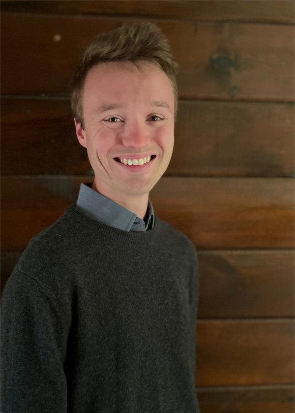 Paul Fink against wall of wood planks, wearing a sweater over a shirt