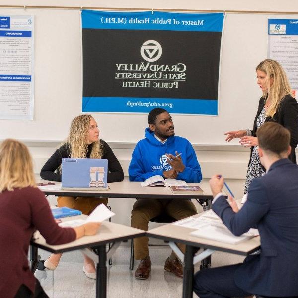 Ranelle Brew stands at the left while students are seated at desks; a banner reads GVSU Public Health