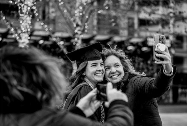  A mother and her daughter wearing a cap and gown take a selfie together. 