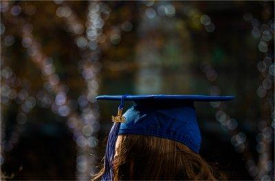 Holiday lights twinkle behind a person wearing a blue mortar board cap and 2024 tassel.