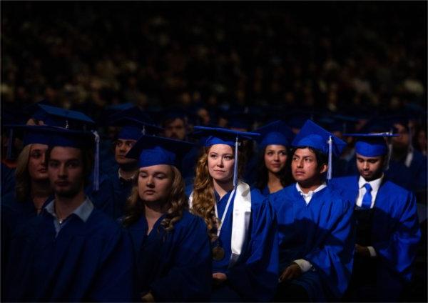  A group of graduates in blue caps and gowns listen to the speaker. 