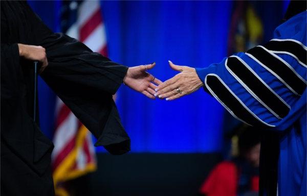  A university president stretches out her hand to shake the hand of a graduate. 