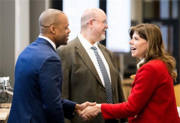 two people shaking hands in foreground, man in back between them