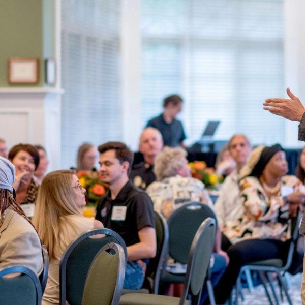 man standing talking to room full of people in the Alumni House who are seated at tables