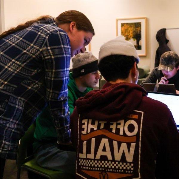 three people looking at a laptop, two seated, one standing