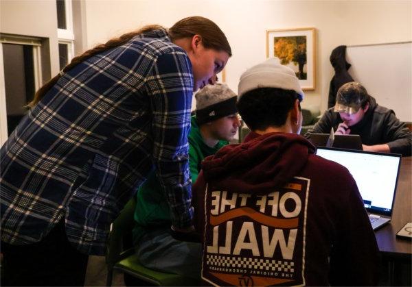 three people looking at a laptop, two seated, one standing