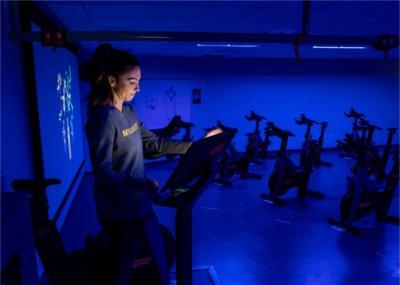 Stacy Connell of Technogym, demonstrates features of the new Technogym group cycle room inside the Recreation Center. The experience uses music, visual effects and performance data to create interactive training.