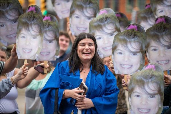  A graduate laughs as they are surrounded by cutout photos of themselves as a preschooler. 