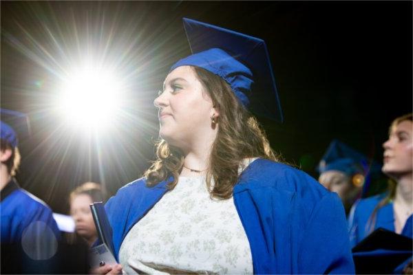  A graduate in blue walks past a beam of light. 