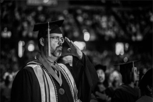  A faculty member in regalia salutes the flag. 