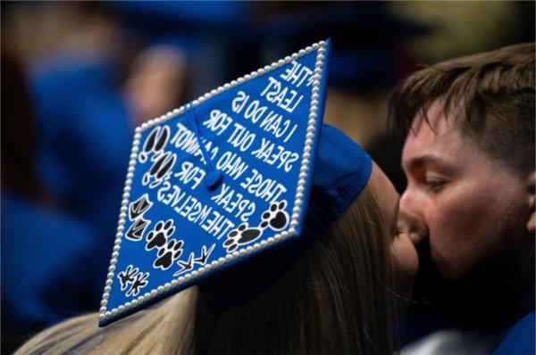  Two graduate kiss while one wears a mortarboard cap. 