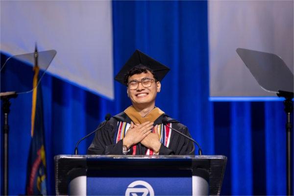   A student speaks at a lectern while putting their hands over their heart.