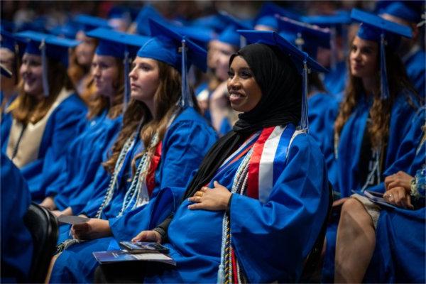  A graduate holds their hand to their belly while wearing a blue cap and gown.