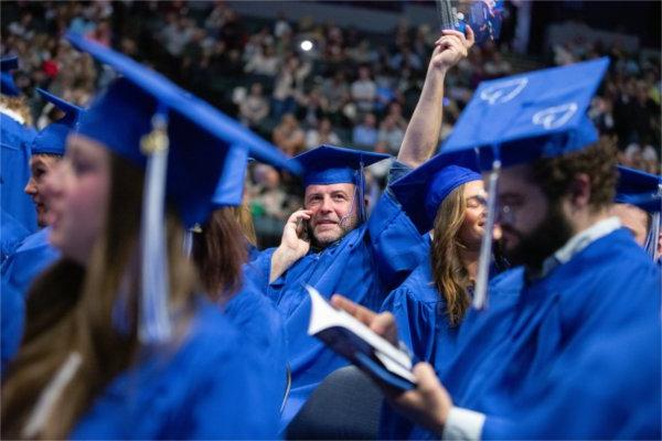  A graduate waves to someone in the crowd while on their cellphone.