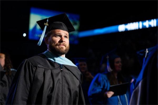  A graduate with a black cap and gown looks proud as they walk in Commencement.