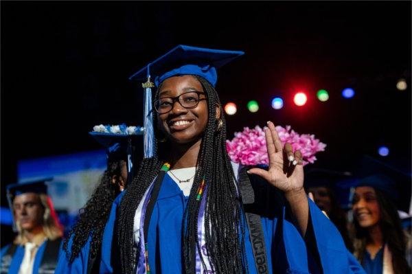  A graduate makes an anchor up hand signal while smiling.