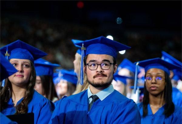  Graduates with their blue caps and gowns listen to a Commencement speaker.