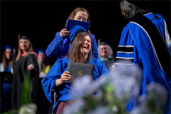  A graduate laughs after their mortarboard cap falls off as they cross the stage. 