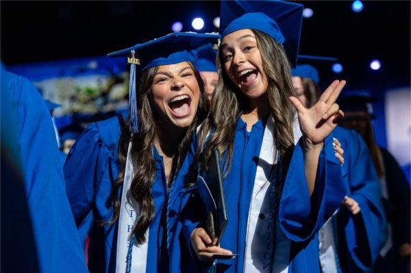   Graduates celebrate as they cross the stage during Commencement with laughs and the anchor up hand sign. 