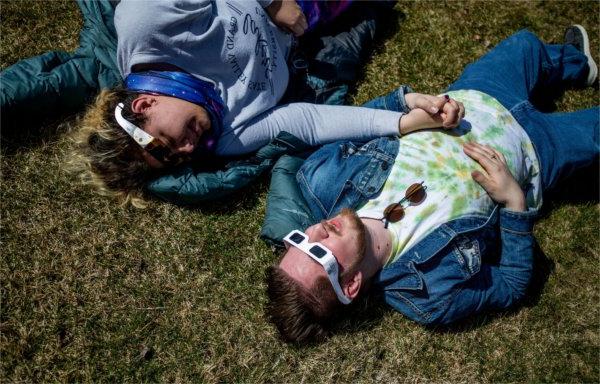  Two students hold hands while wearing protective glasses to view the eclipse.