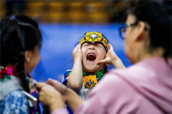  A child wearing colorful regalia laughs. 