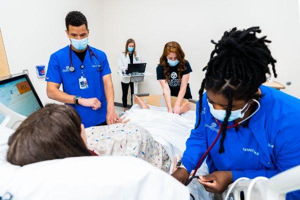 Physician assistant, nursing and occupational therapy students work in a sim lab with a mannequin.