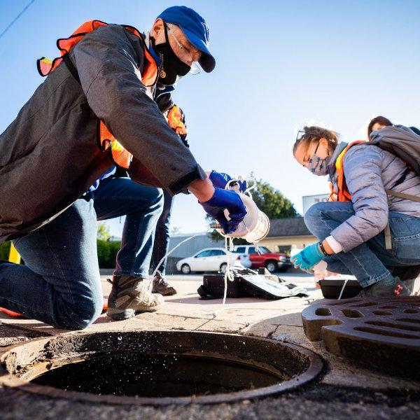 Researchers retrieve a water sample through a hole in the street used for maintenance.