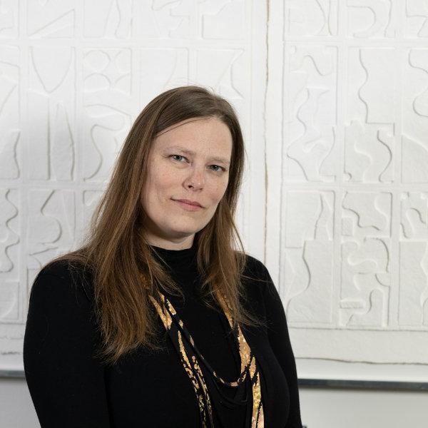 A person slightly smiles while standing before a white background.