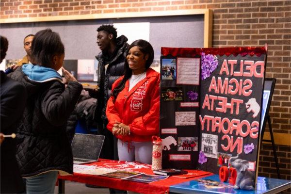 A student stands at her student organization's table during the Blackout event, talking with other students. 