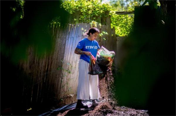 student in white sweatpants and blue t-shirt with GV logo and I VETS on it holds a bag of mulch to spread