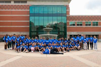 large group of students, faculty and staff members dressed in blue t-shirts and posing in front of the Student Services Building fountain