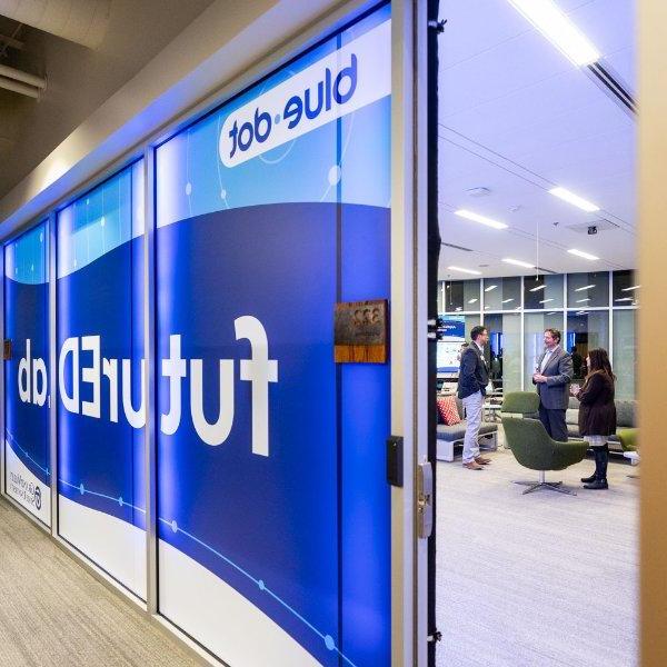 A sign with different shades of blue is seen in windows to a glassed-in office area. The signs contain the words "blue dot" and "futureEDlab."