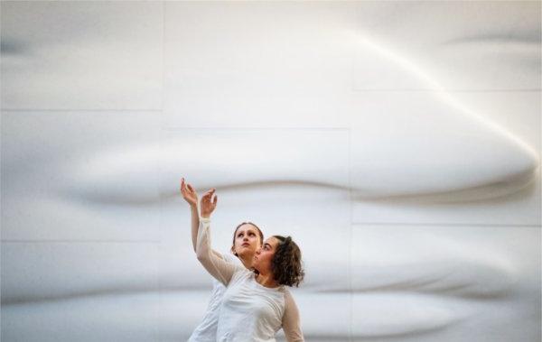  Two dancers wearing while perform in front of a white face sculpture. 