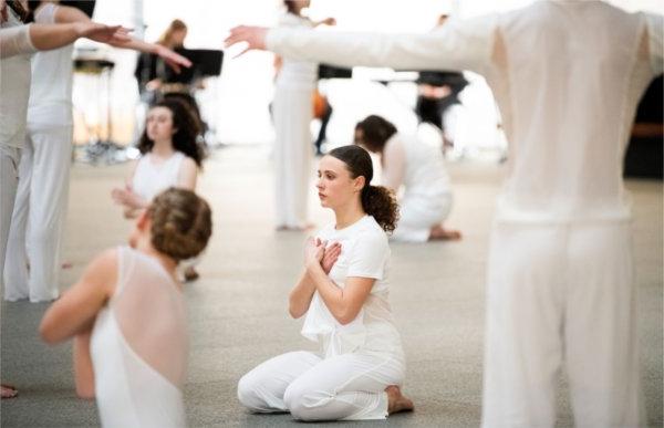  A dancer holds their hands to their heart while surrounded by other dancers wearing white. 