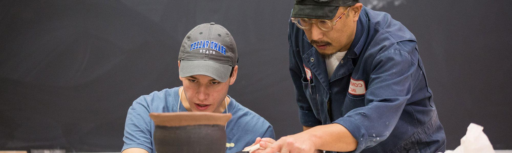 Photo of GVSU studio art student working with his professor in a sculpting class.